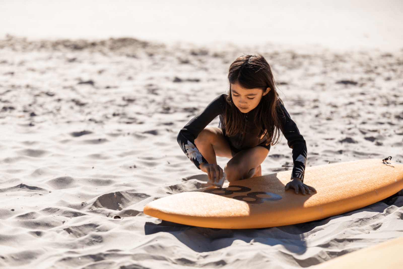Young girl waxing her surfboard at Cocoa Beach, Florida