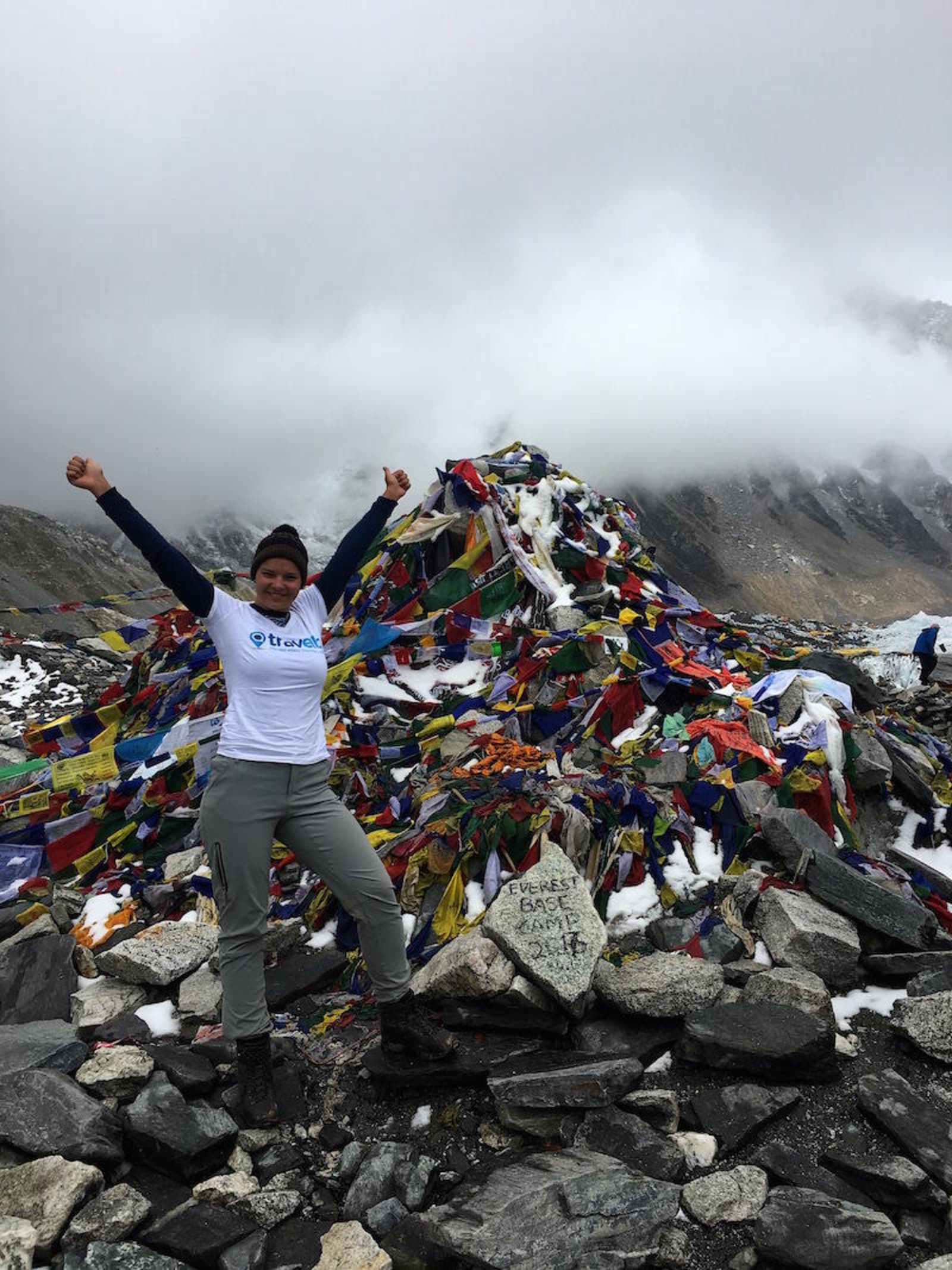 Hiker standing at the Mount Everest base camp, with a large pile of flags in the background