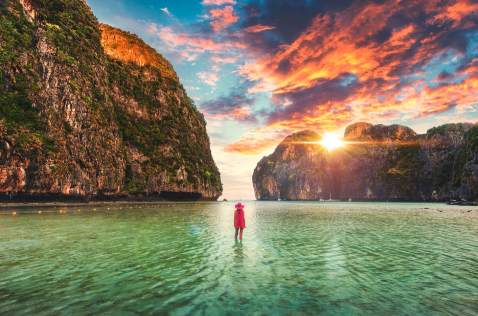 traveller in red paddling in clear waters surrounded by impressive cliff faces.