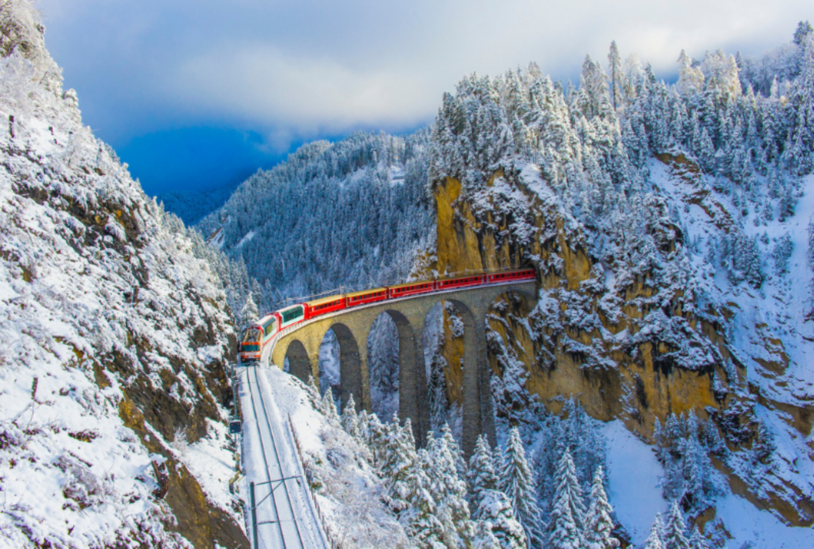 Train above tall bridge in snowy mountain landscape in europe