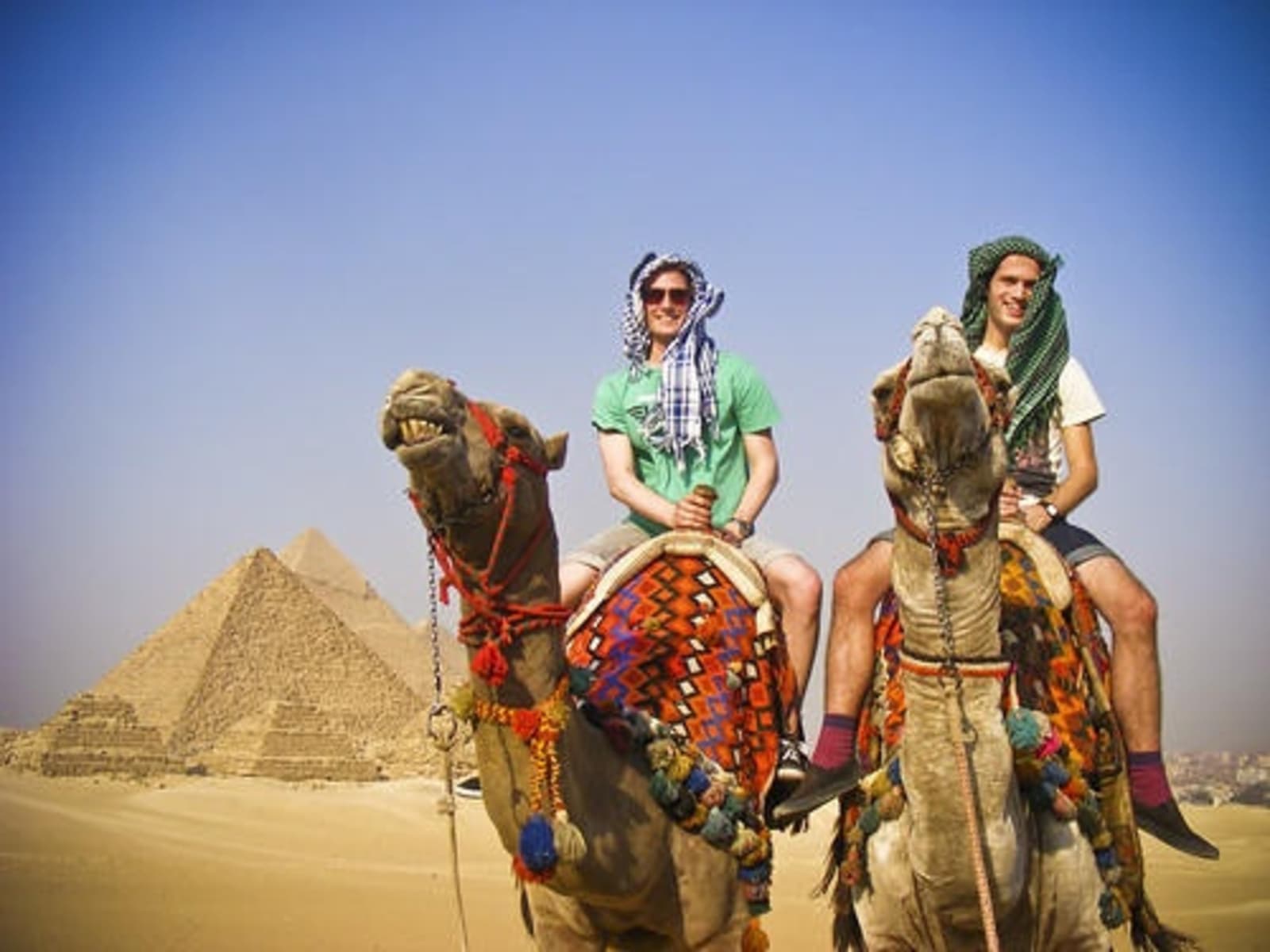 Man and woman riding camels in front of the Pyramids.