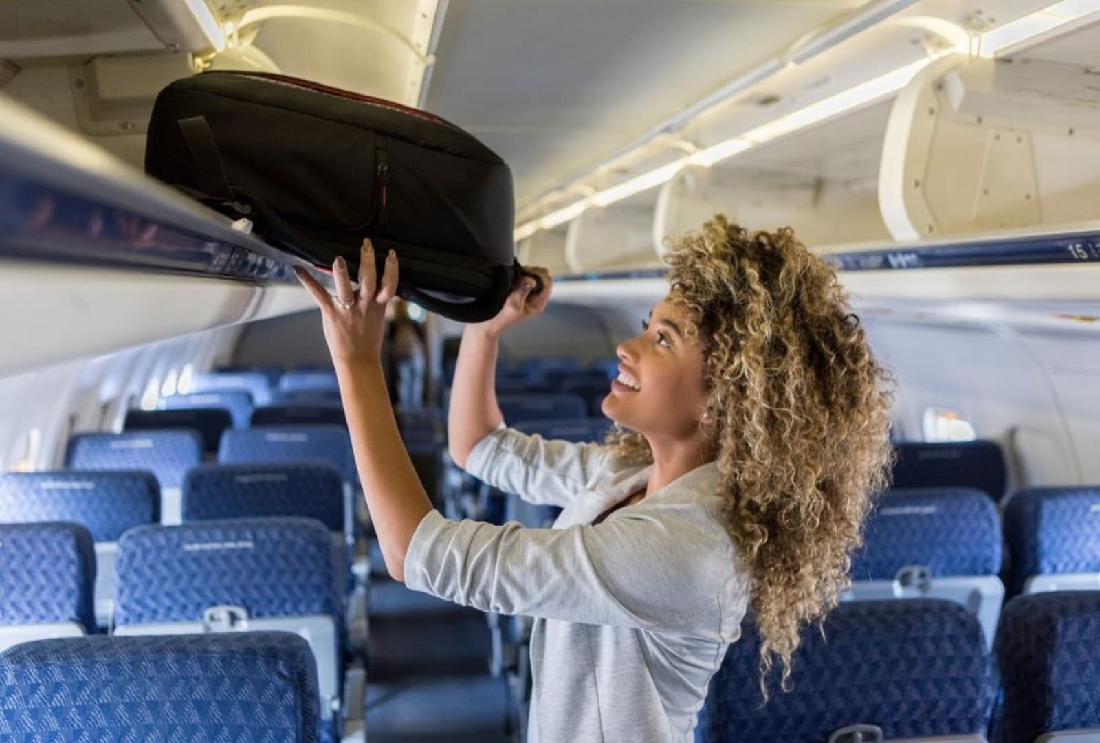 Person loading carry-on bag onto overhead lockers