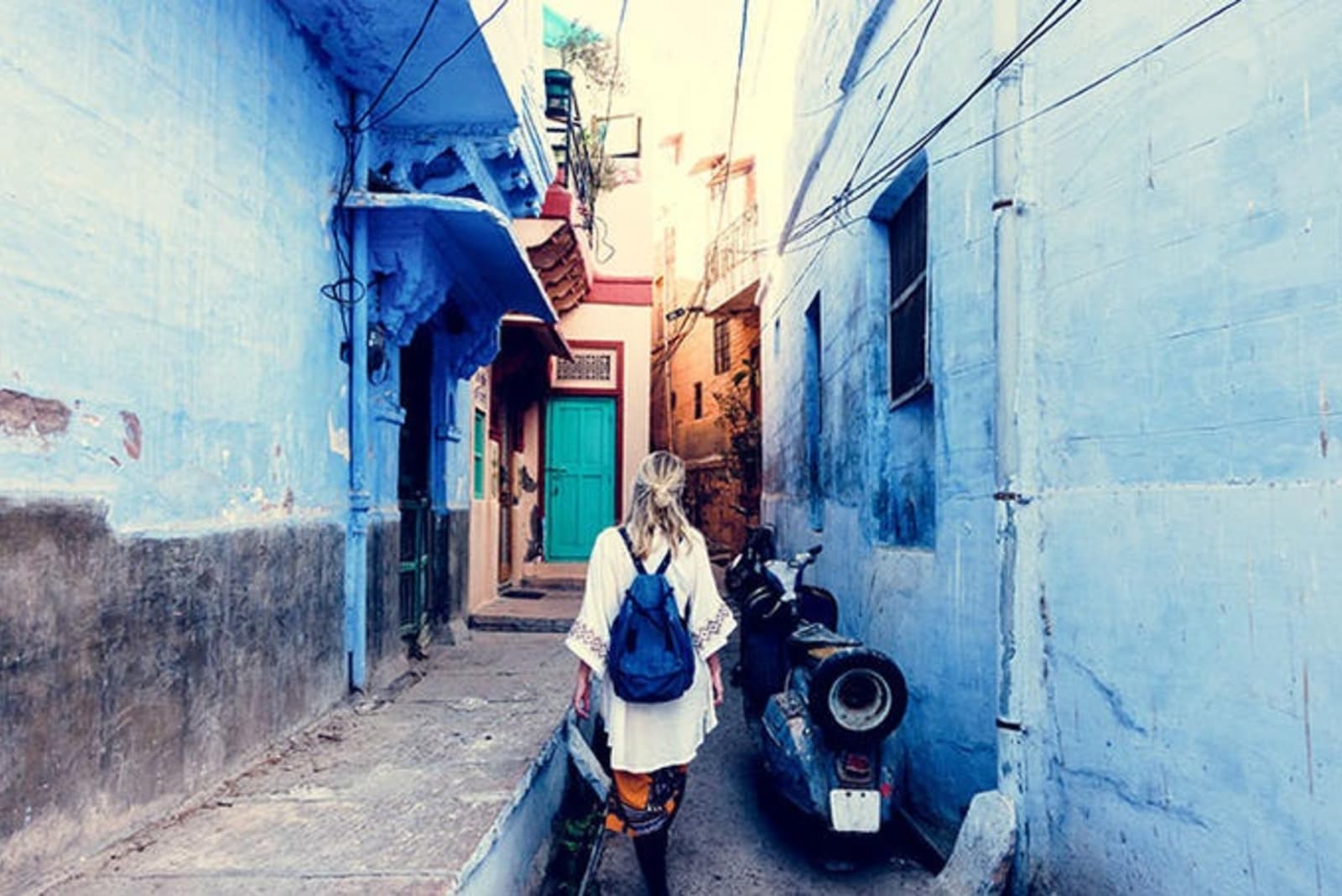 Image of the back of a woman walking through a blue painted alleyway.