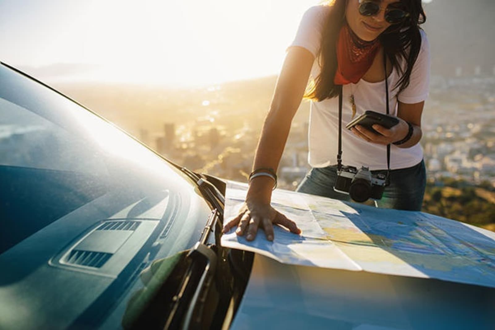 Woman looks at a map resting on the bonnet of a car.