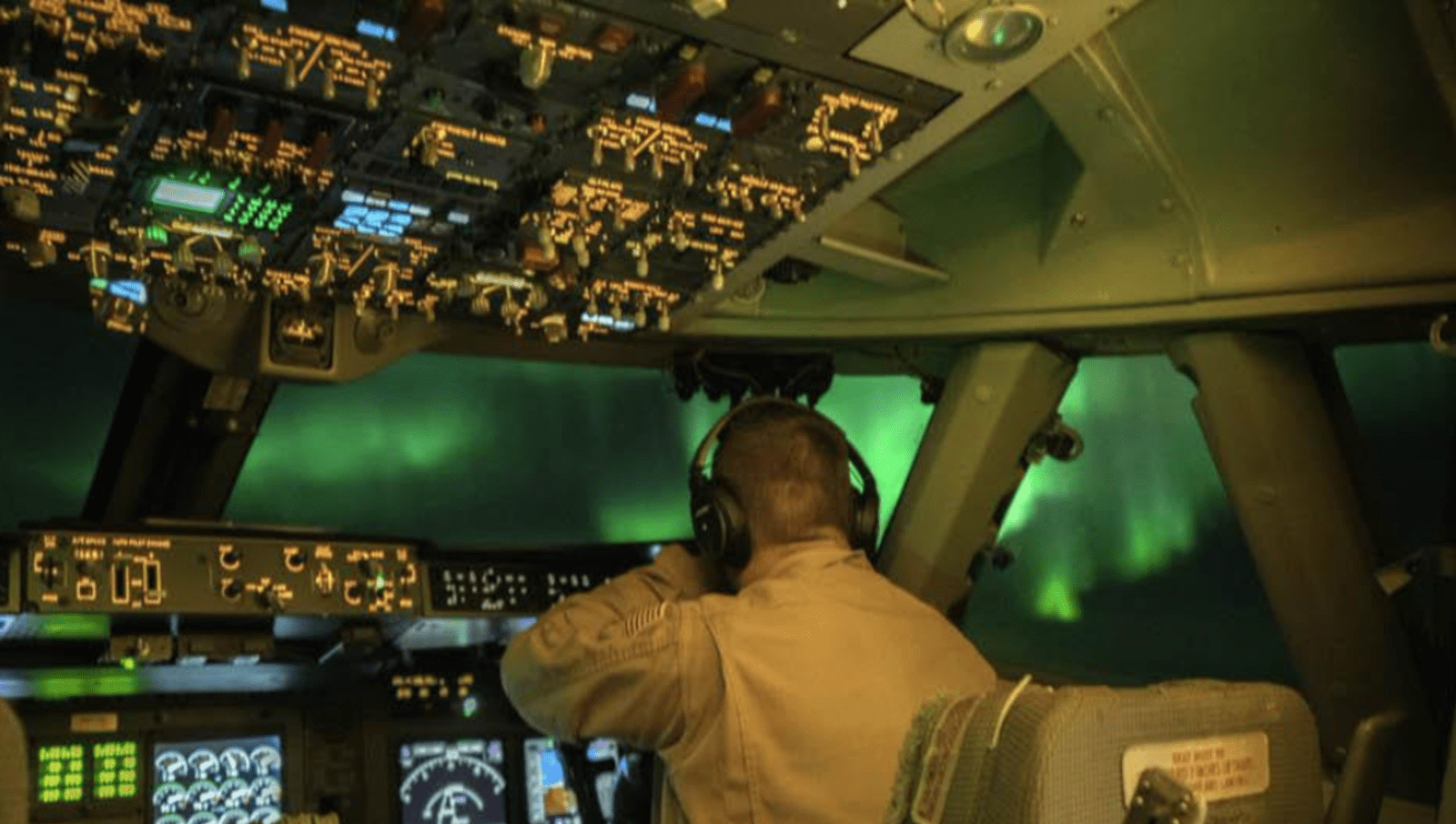 Pilot in plane cockpit with Aurora Australis in front of window 