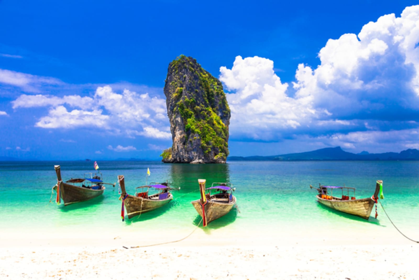 four boats on the beach of Krabi with large rock in background