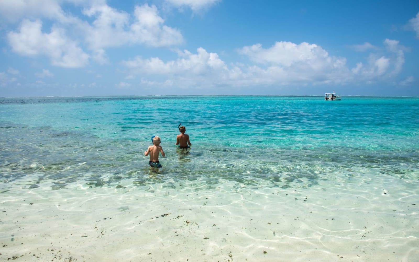 A pair of people wading out in clear blue water to go snorkelling