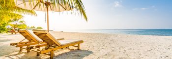 Beach chairs sat on a beach with sun glaring through beach umbrella