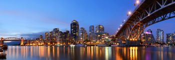 City view under Vancouver bridge with lights reflecting off river water during dusk