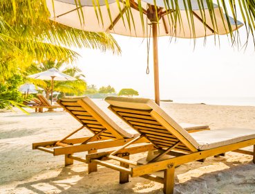 Beach chairs sat on a beach with sun glaring through beach umbrella