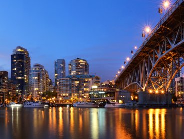 City view under Vancouver bridge with lights reflecting off river water during dusk