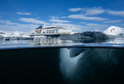 Expedition ship anchored among icebergs viewed half underwater showing ice floating beneath the surface