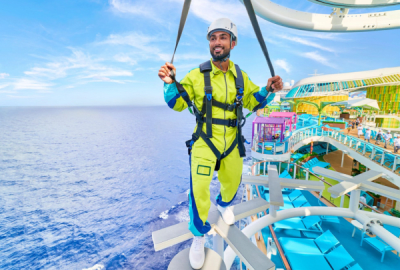 Man ziplining high above Icon of the Seas with colourful waterslides and pools spread out below