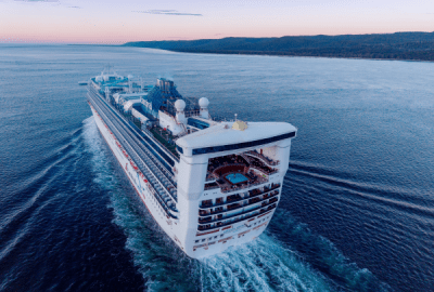 Carnival Encounter cruising along a calm coastline leaving a long white wake at dusk