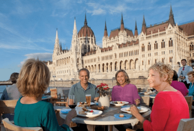 Friends dining on a river cruise deck overlooking the illuminated Hungarian Parliament Building in Budapest