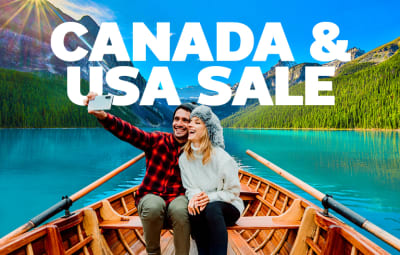 A couple enjoying a canoe ride on a turquoise lake surrounded by forested mountains in Canada, smiling and taking a selfie under clear blue skies and scenic outdoor adventures in North America.