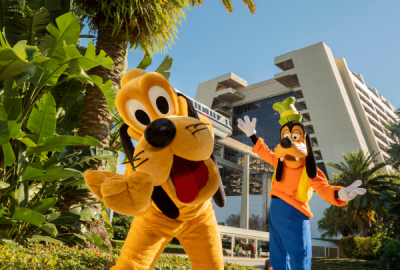 Pluto and Goofy posing playfully among palm trees outside Disney's Contemporary Resort