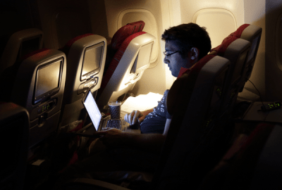 A man looking at laptop, on an aircraft.