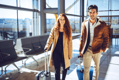 Smiling couple wheeling suitcases through a sunlit airport terminal ready for their business trip