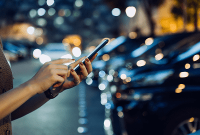 Woman checking her phone on a city street at night surrounded by blurred car lights