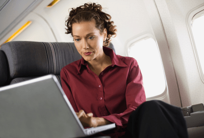 A woman working on a laptop while seated in a business class airline seat