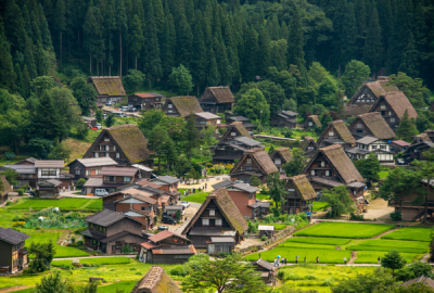 Aerial view of Shirakawa-go village in Japan, with traditional gassho-zukuri thatched-roof farmhouses surrounded by rice fields and forested mountains
