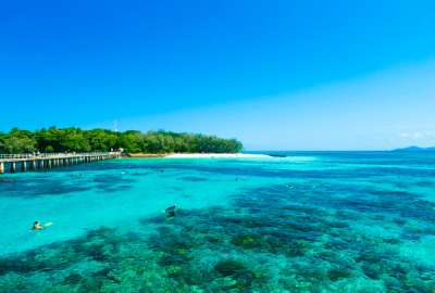 Snorkellers exploring the crystal-clear turquoise waters of the Great Barrier Reef off a tropical island with a white sand beach and timber jetty