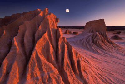 The full moon rises while the sun sets simultaneously at the ancient sandstone rock formations known as the Walls of China at Mungo National Park