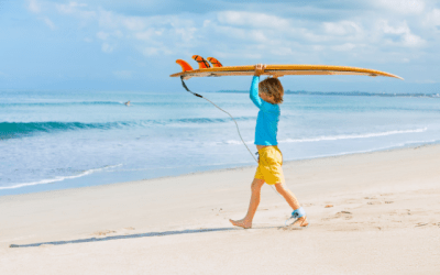 Young boy on a beach carrying a surf board into the ocean