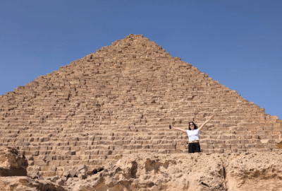 A woman waves while standing at the base of one of the Pyramids of Giza