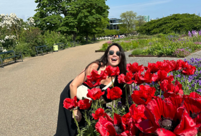 Sara smiles by a bloom a of big red flowers at the Rosenborg Gardens in Copenhagen