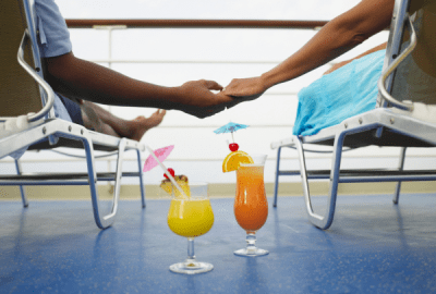 A couple lie in deck chairs holdings hands with cocktails