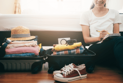 A woman marks off a checklist with items stacked in a suitcase