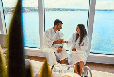 A couple in bathrobes share a drink inside a cruise ship