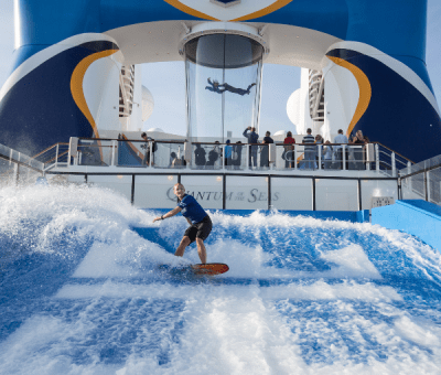 A woman rides the Surf-rider with two people in a skydiving simulator onboard a cruise ship