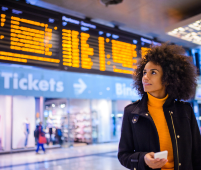 A woman at an airport checks flight times on an overhead digital display