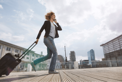 Woman on the phone walking with a rolling suitcase in the city