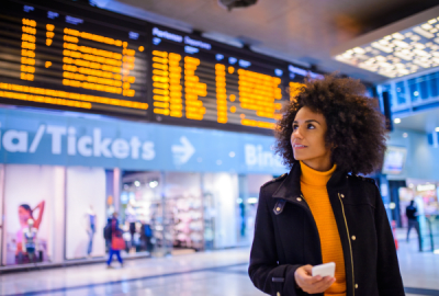 A person checks an overhead digital flight schedule at an airport terminal