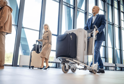 A man walks through an airport pushing a cart full of suitcases