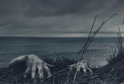 Dirty, spooky hands reach over the top of a desolate sea cliff.