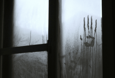 A ghostly handprint drips down a foggy window