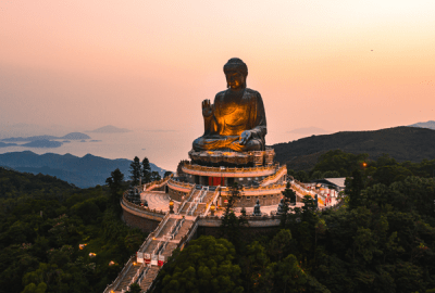 The giant bronze Buddha at Po Lin Monastery towers over hills and islands at sunset