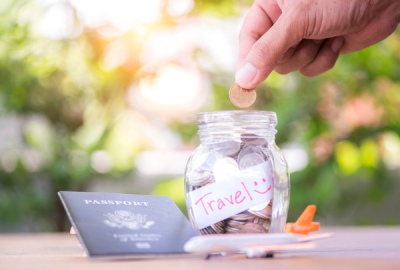 A hand drops a gold coin in a jar marked "travel"