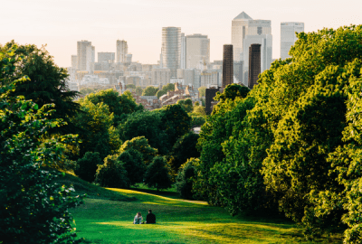 A couple sit in Greenwich Park, London looking the Canary Wharf 