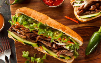 Vietnamese banh mi baguette sitting partially open on a wooden chopping board.