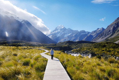 Girl walking on boardwalk at Hooker Valley Track, with view of Mount Cook.