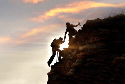 Two silhouetted hikers scaling a cliff