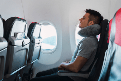 A man is seated in an aircraft wearing a bulky neck pillow