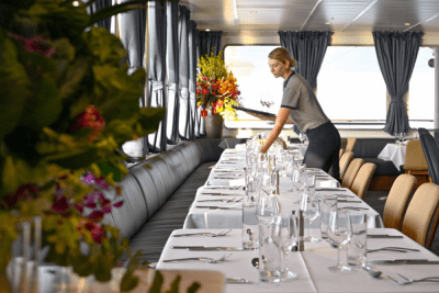 A woman sets places at a dining tables aboard a small cruise ship