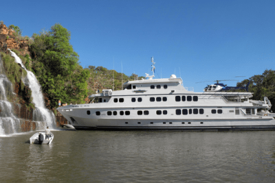 A small cruise ship anchors by a waterfall in Kimberley, Western Australia